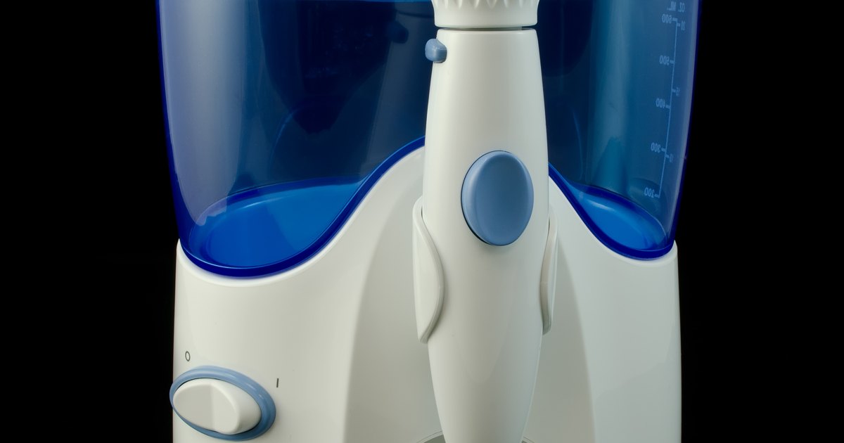A white countertop water flosser with a blue-tinted reservoir and handle rests against a white background.