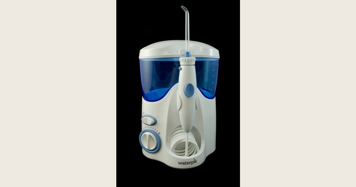 A countertop water flosser with a reservoir, hose, handle, and tip.