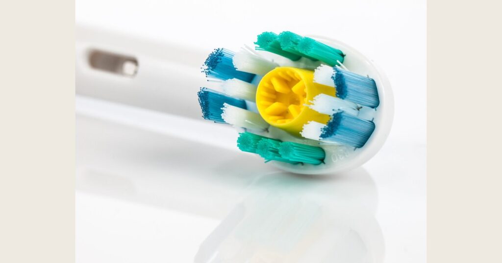 Close-up of an electric toothbrush head with blue and teal bristles around a yellow center.