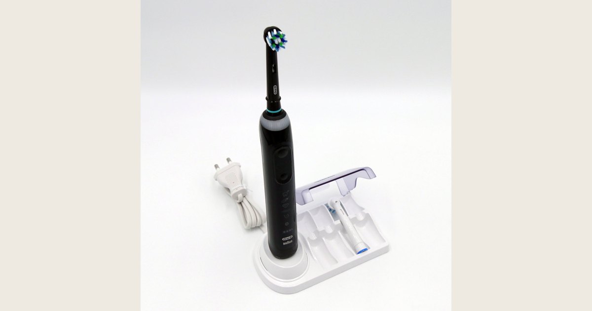 A black Oral-B electric toothbrush beside a white charging stand and plug.